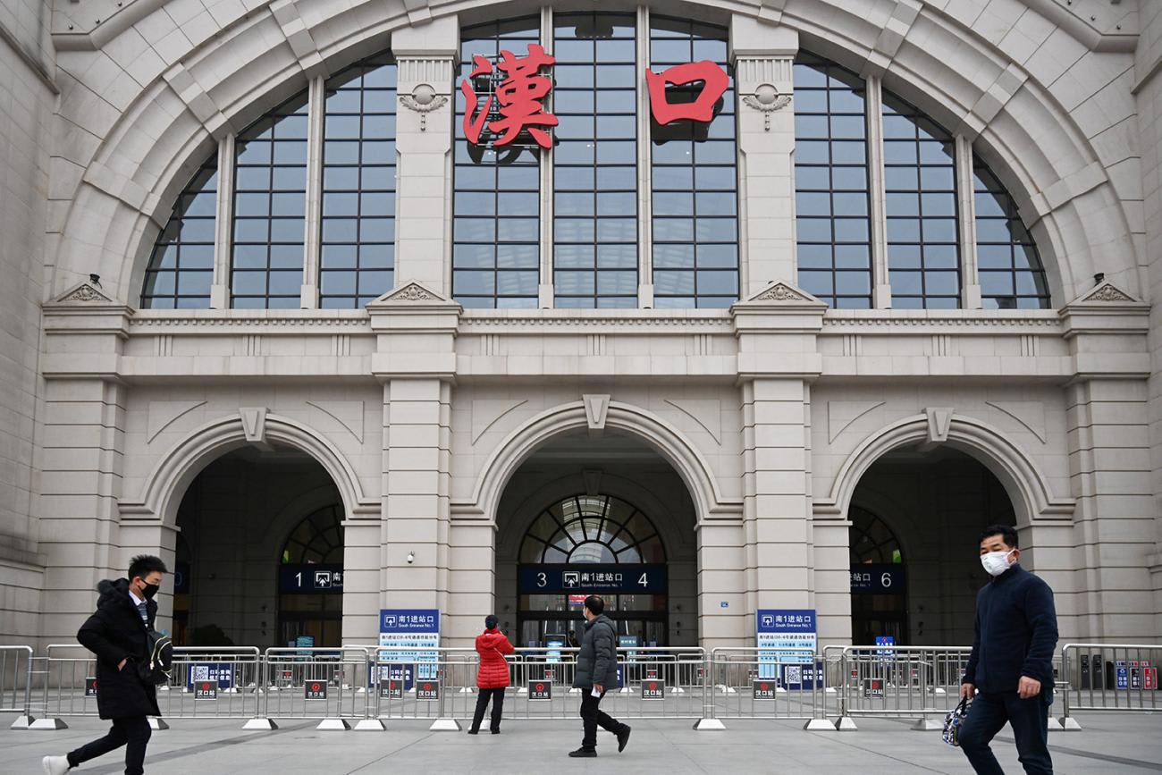 The picture shows just a few people walking in front of the grand entrance to a huge terminal building. Metal gates bar the entrance.