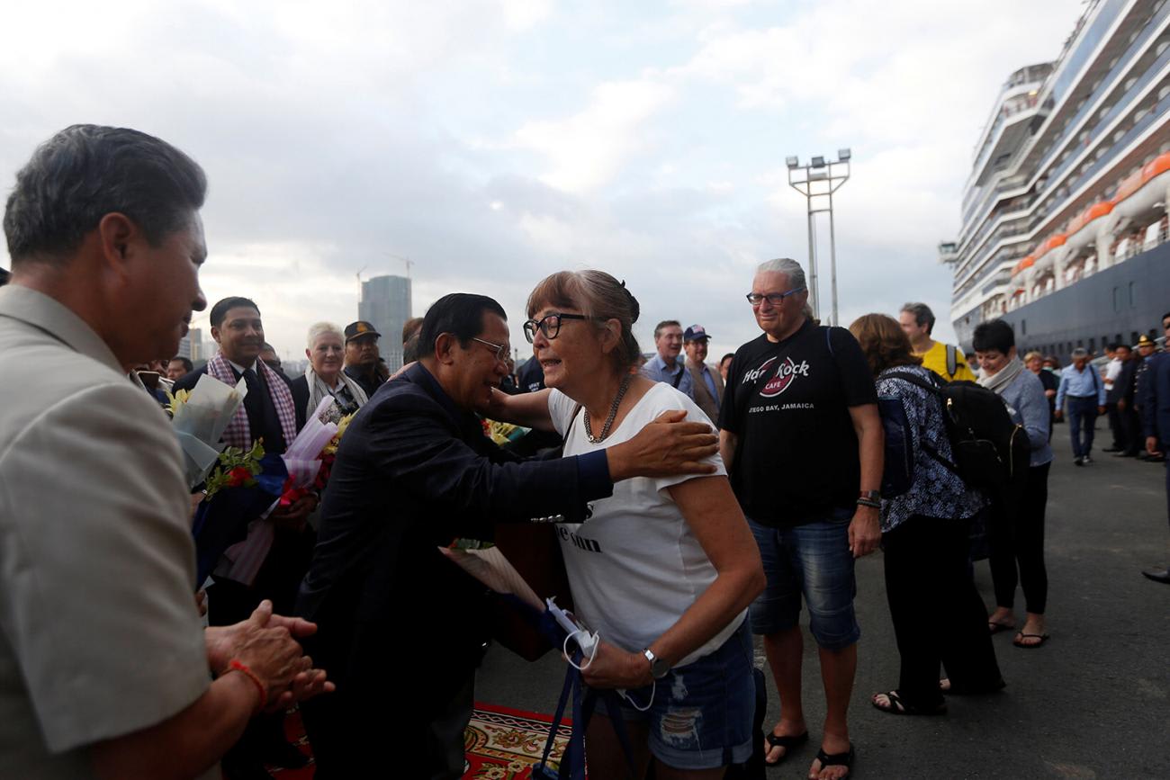 Picture shows the ship docked and disembarked passengers being greeted by the PM. He is going in for a hug with one lady.
