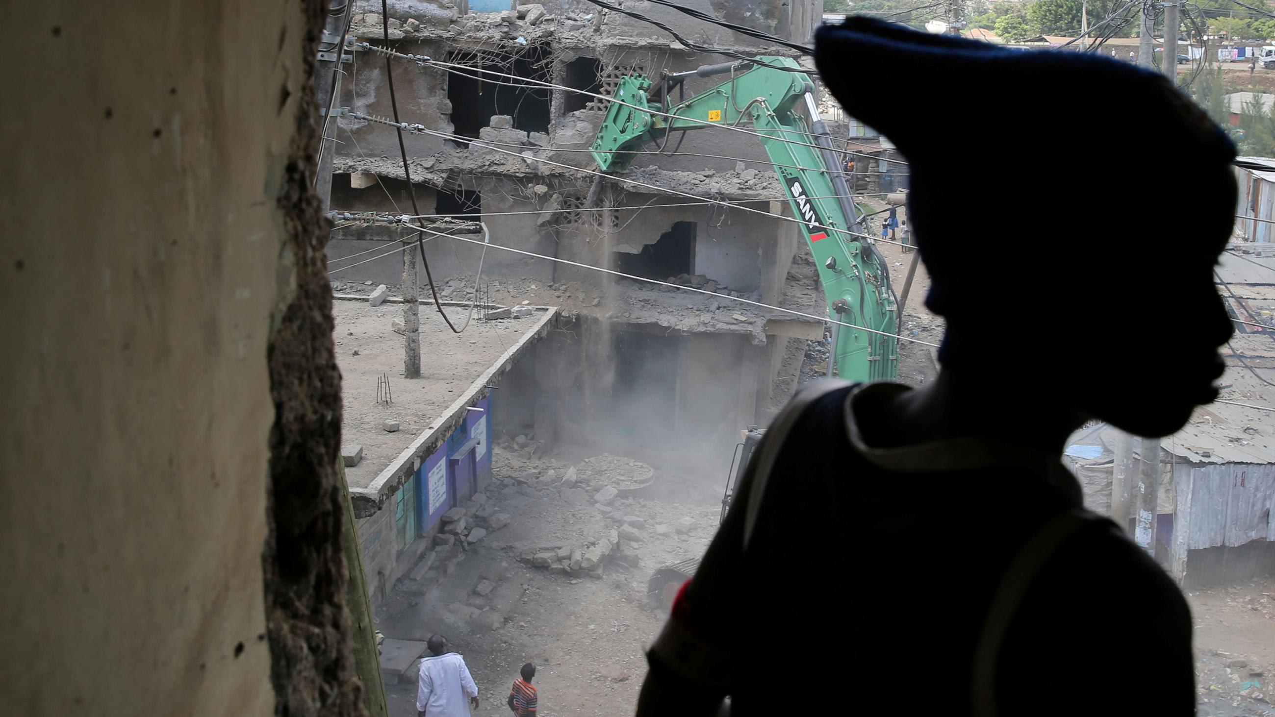 Image shows a building being torn down while the boy watches. He is silhouetted in the foreground.