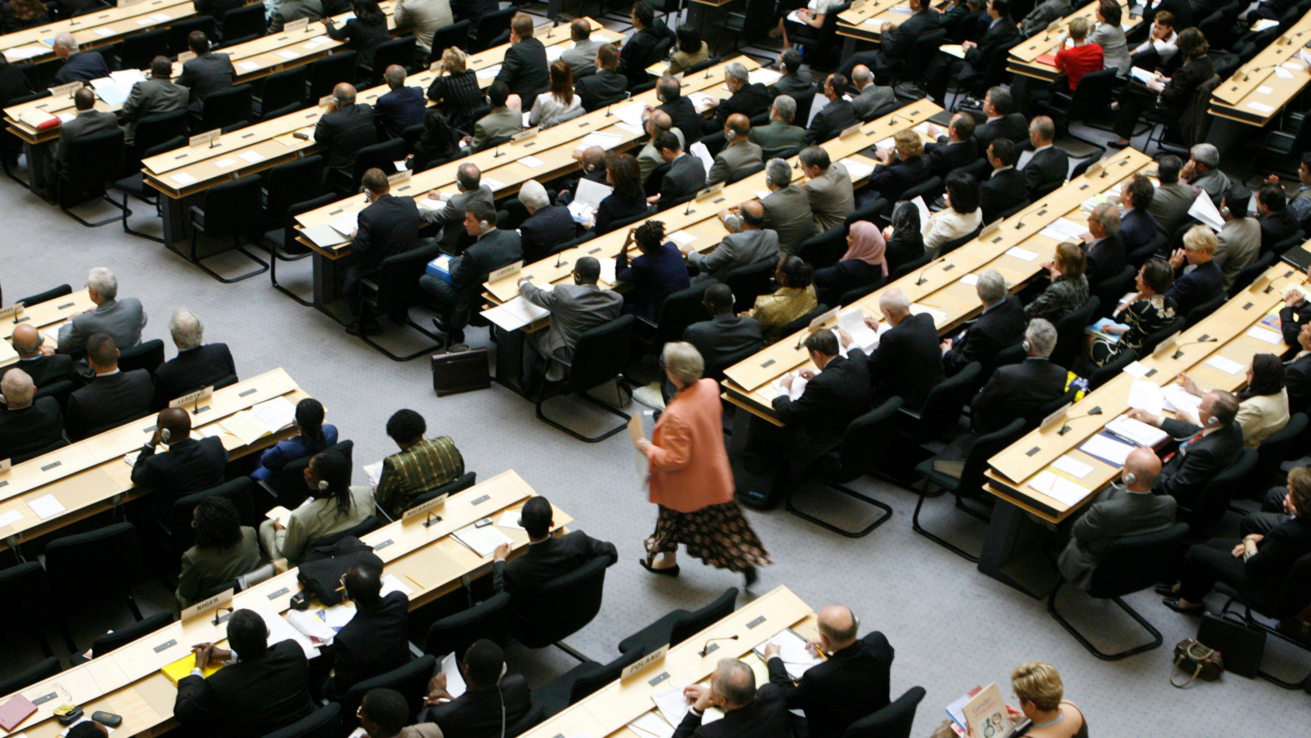 The photo shows a delegate walking up the aisle of a crowded assembly hall.
