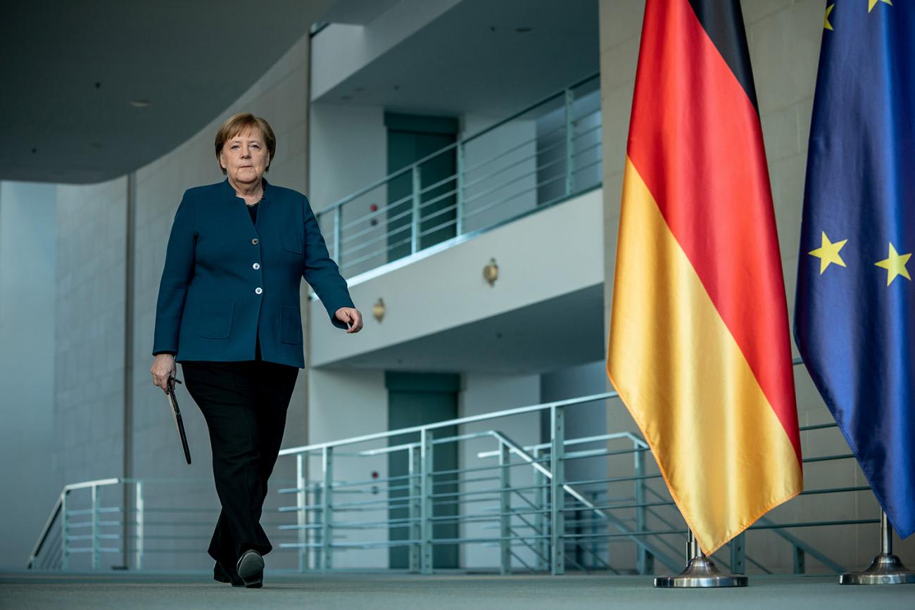 The photo shows the German leader walking through a building interior next to a German flag.
