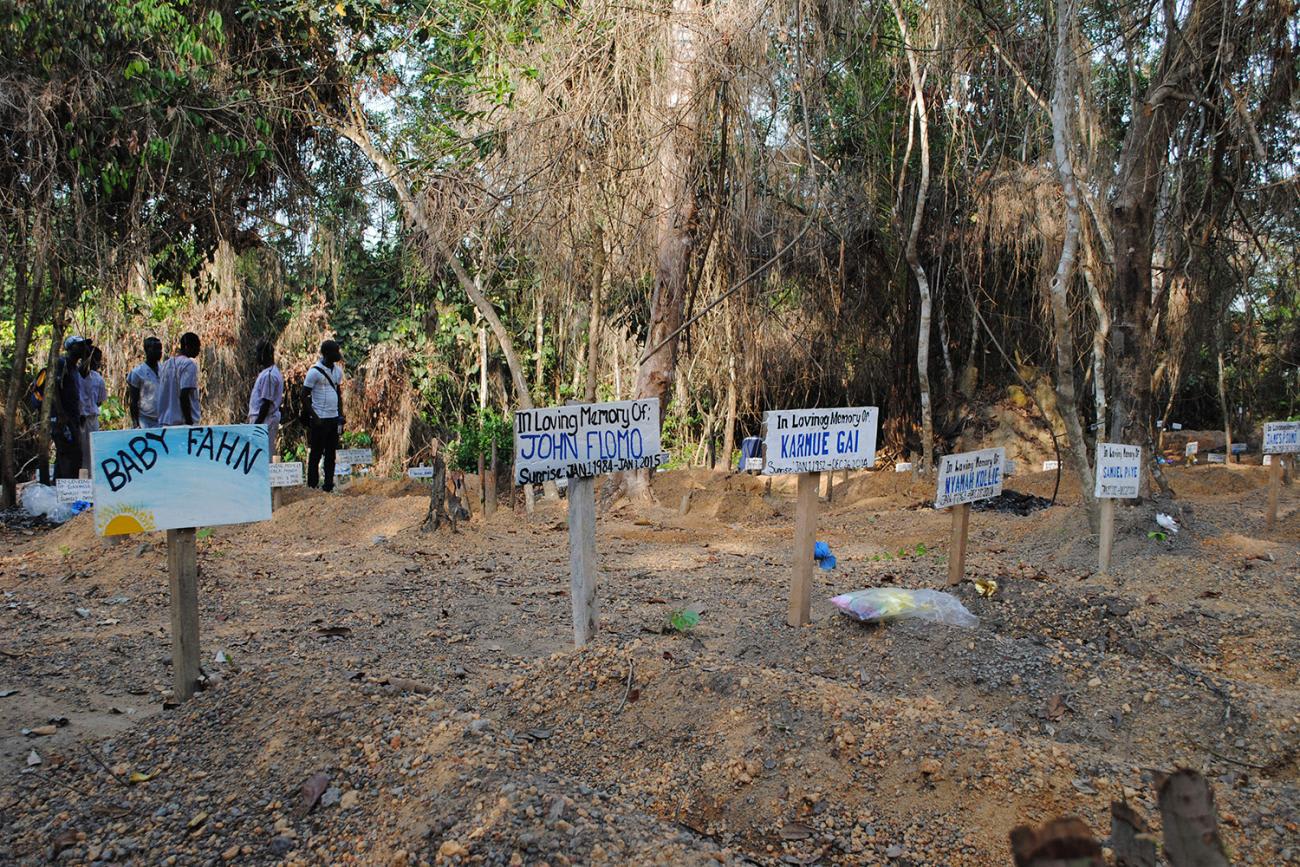 The graveyard has what appear to be freshly dug graves adorned with hand-painted wooden markers with names like "John Flomo" And "Baby Fahn."