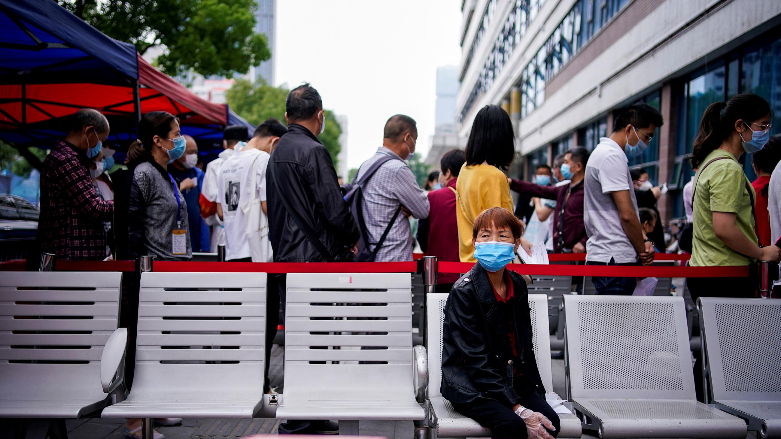 The photo shows a woman sitting on the back side of a barricade along which people are lined up.