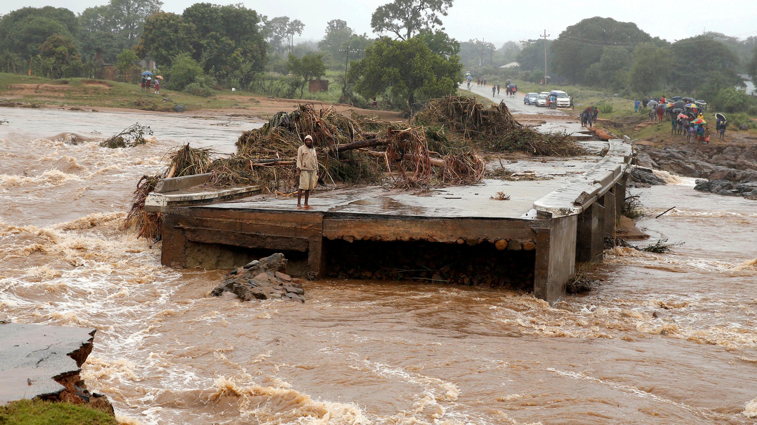The photo shows a man at one end of a bridge that is completely washed away from the flooding.