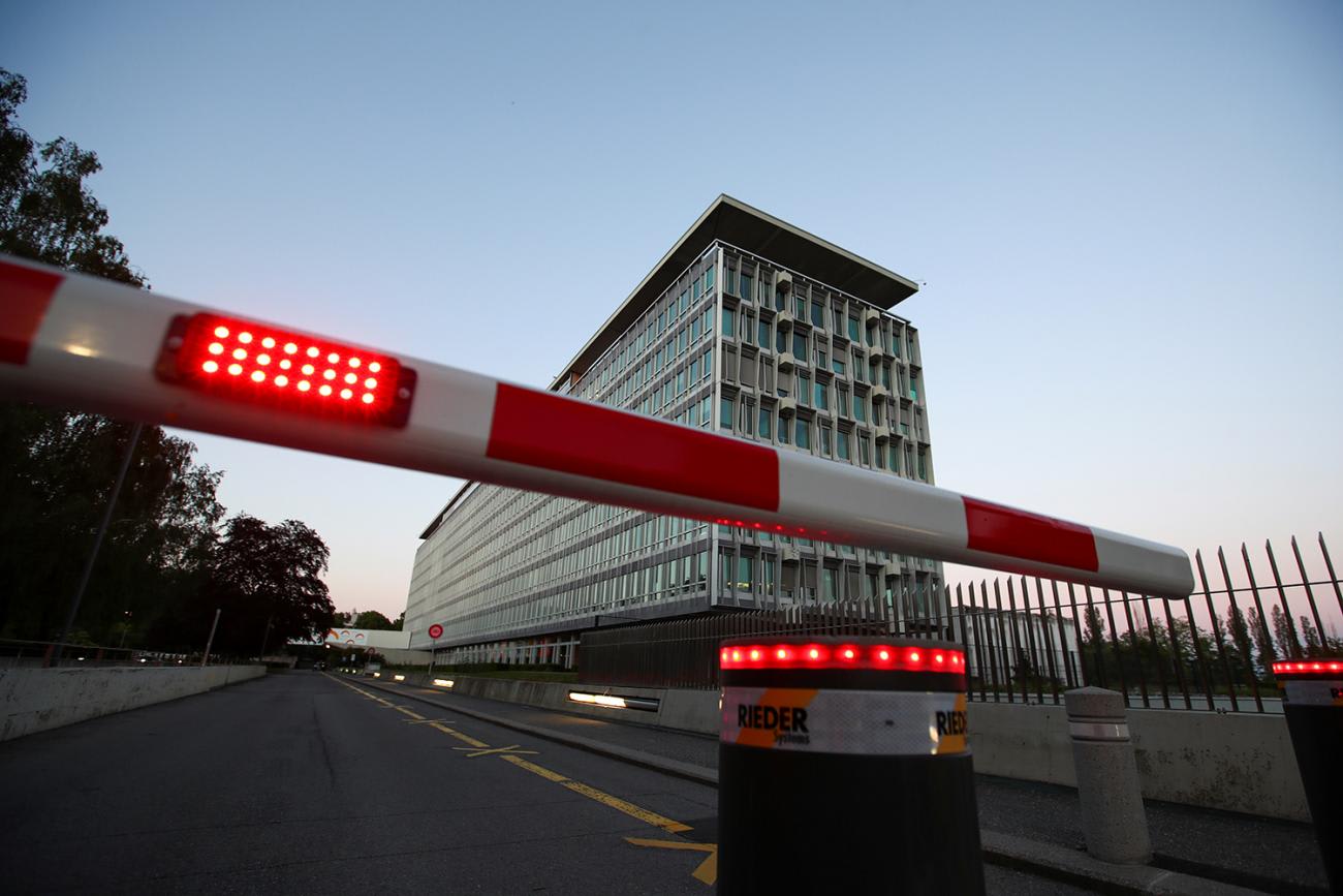 The photo shows the WHO building at night with a red and white guard barrier lowered to block the street entrance.