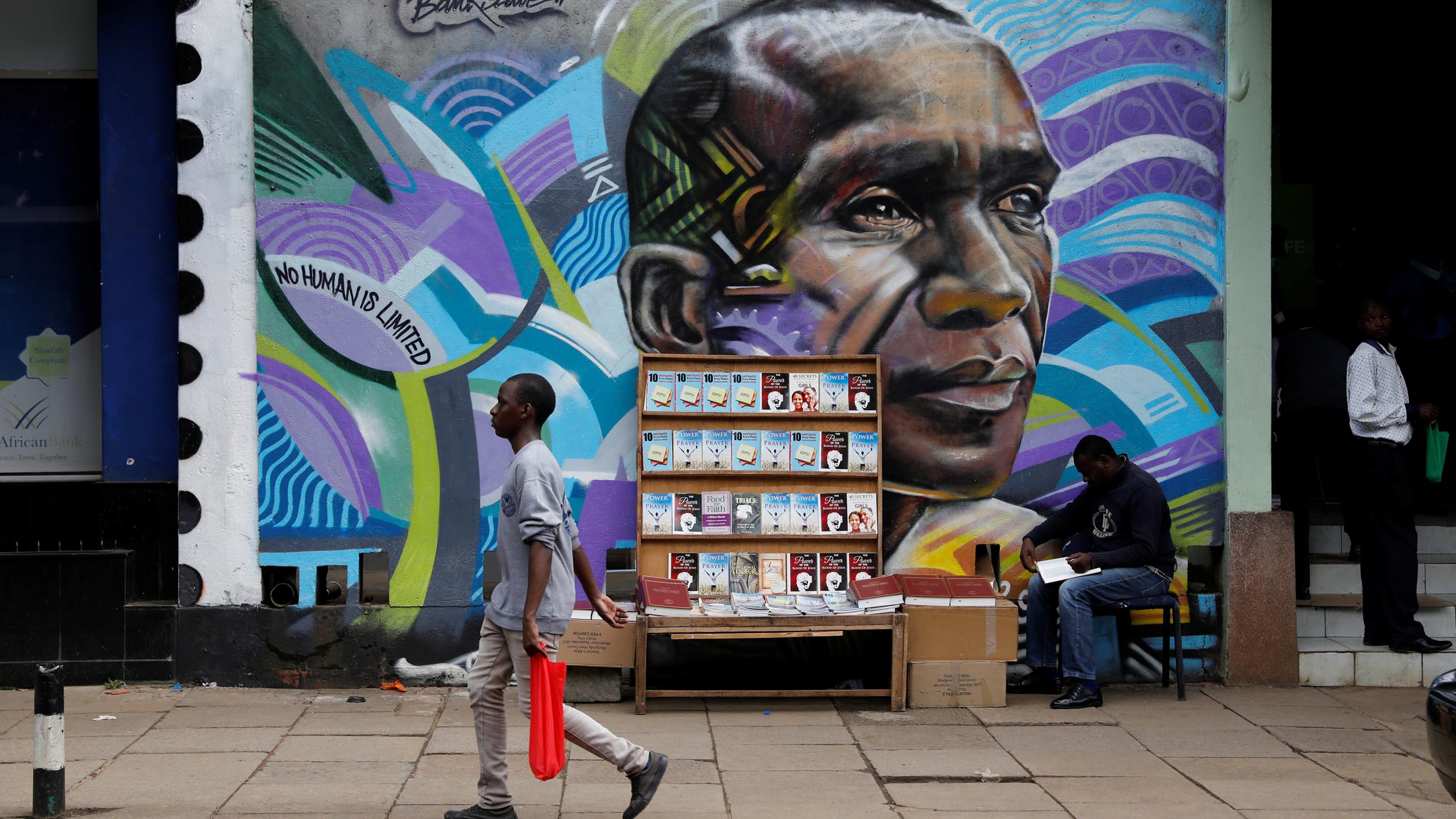 The photo shows a man walking past a huge mural of the marathoner with a street vendor standing in front.