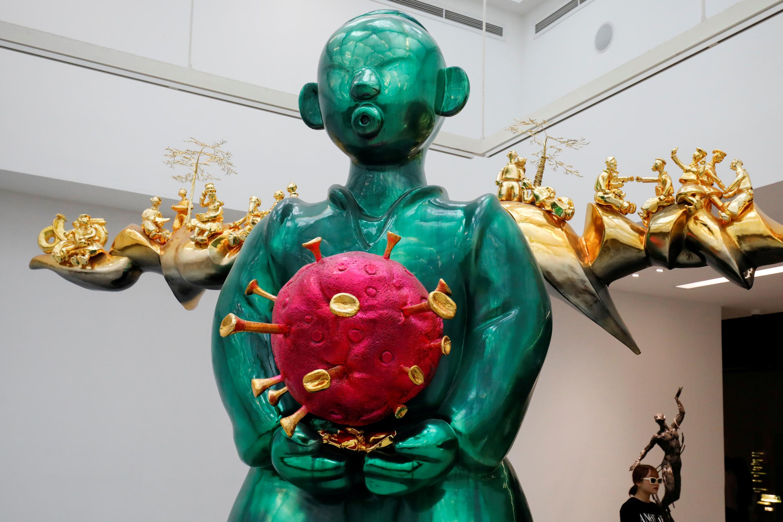 A visitor poses near a green, red, and gold coronavirus-shaped sculpture by artist Pham Thai Binh during an art exhibition at Vincom Center for Contemporary Art in Hanoi, Vietnam, on October 12, 2020.