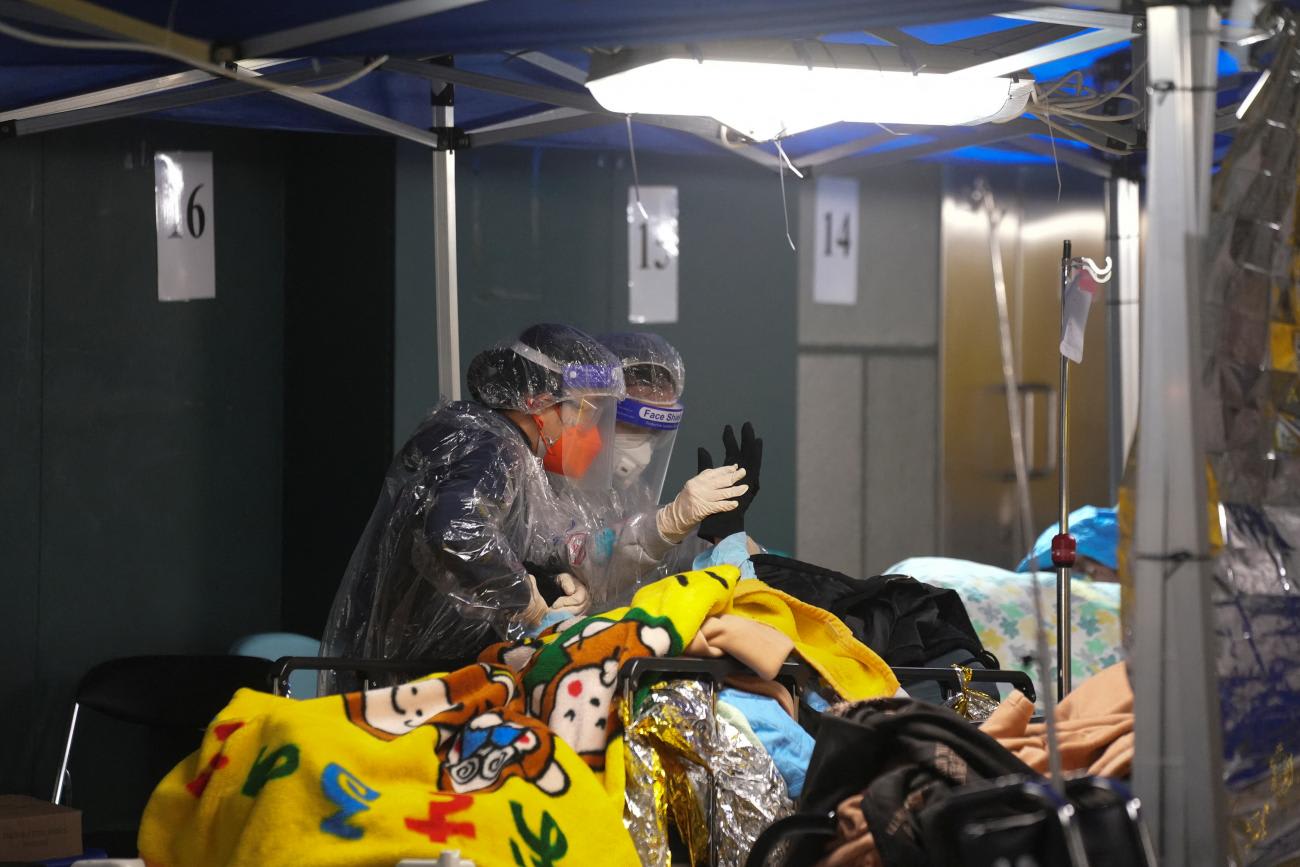 A woman holds the hand of a patient at a makeshift treatment area outside a hospital, during the COVID outbreak in Hong Kong, on February 17, 2022.