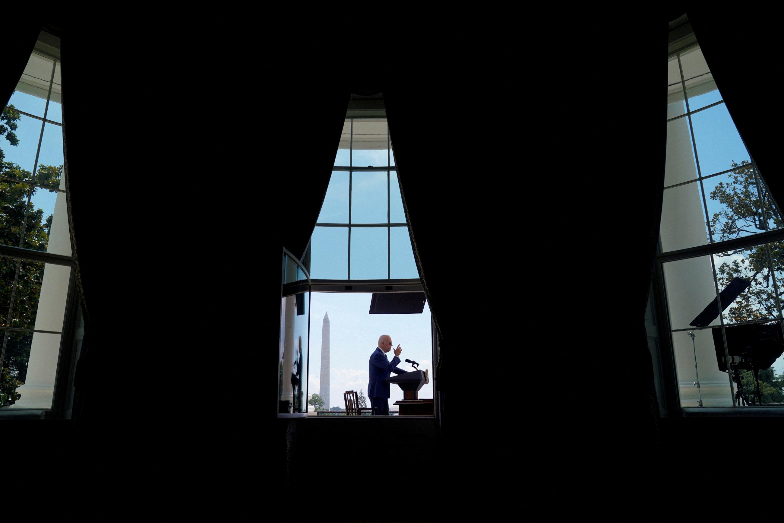 U.S. President Joe Biden is seen in silhouette through a window of the White House, with the Washington Monument in the background, as he speaks before signing two bills aimed at combating fraud in the COVID-19 small business relief programs at the White House in Washington, DC, on August 5, 2022.