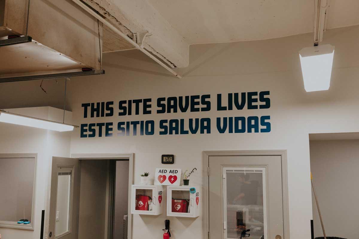 A wall reads "This site saves lives" in English and Spanish.