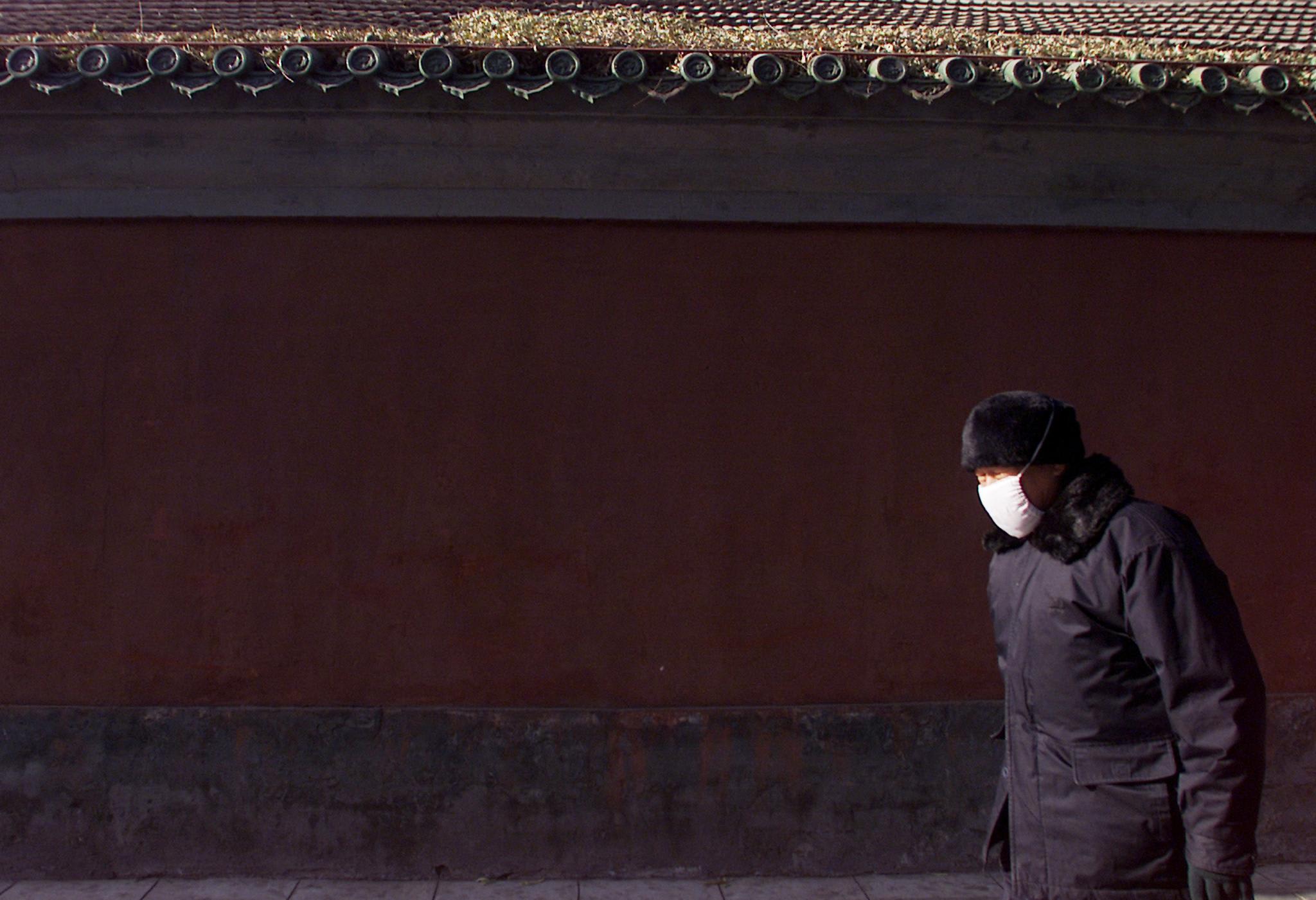 An elderly Chinese man, bundled up for freezing temperatures, walks past an old building, in Beijing, China, on December 9, 2002.