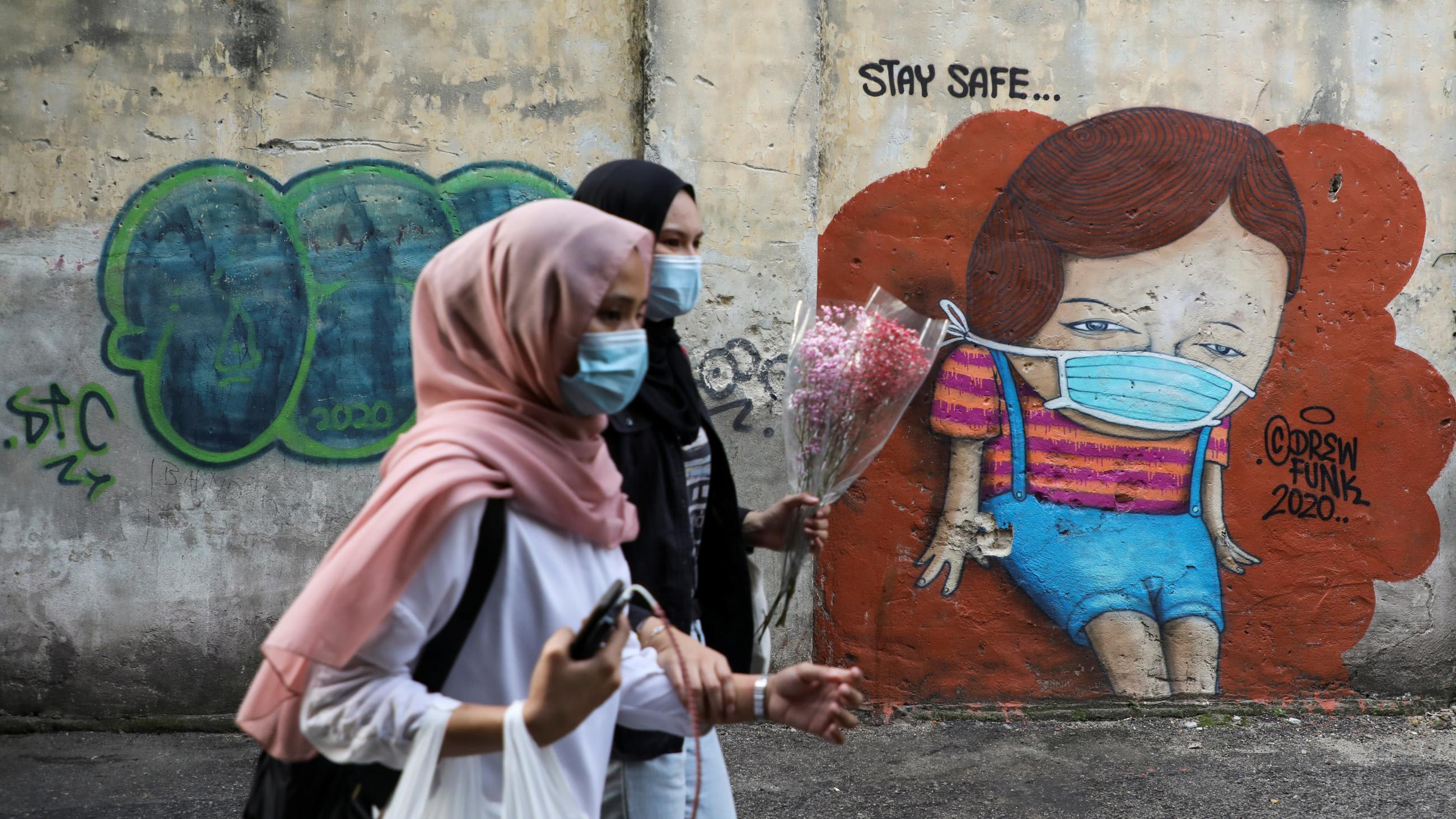 Women wearing protective masks walk past street art encouraging people to 
