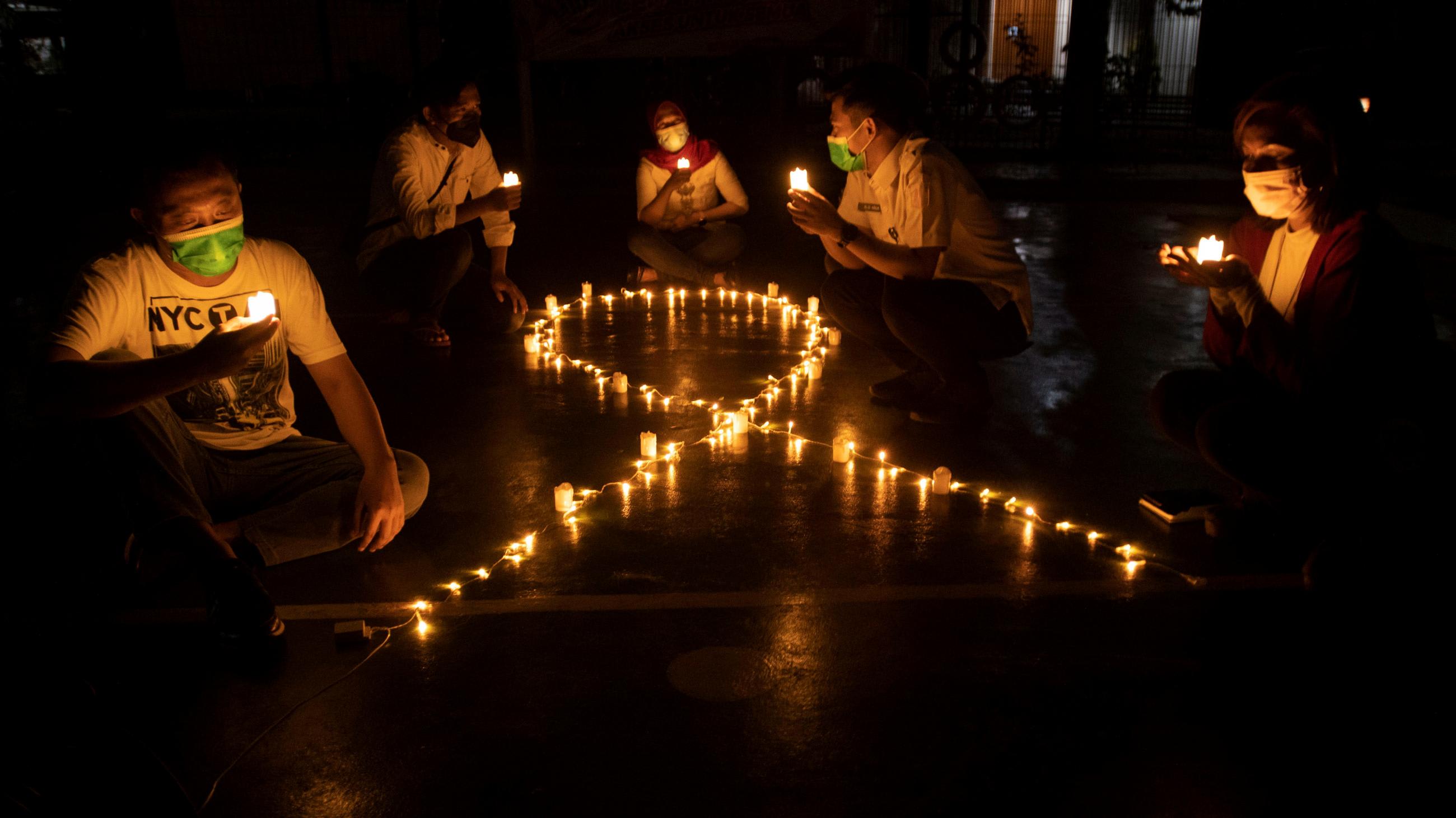 Activists sit next to candles laid out in the shape of an AIDS ribbon, commemorating World Aids Day in Jakarta, Indonesia, on December 1, 2021.