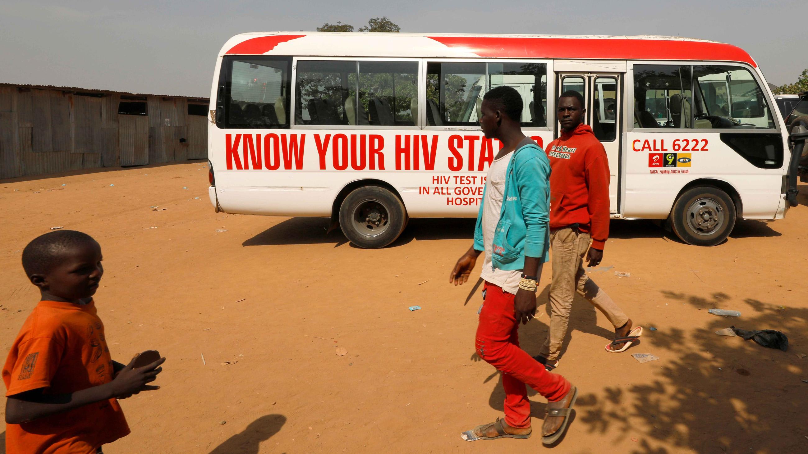 People walk past a bus during an HIV/AIDS awareness campaign on the occasion of World AIDS Day at the Kuchingoro IDPs camp in Abuja, Nigeria, December 1, 2018.