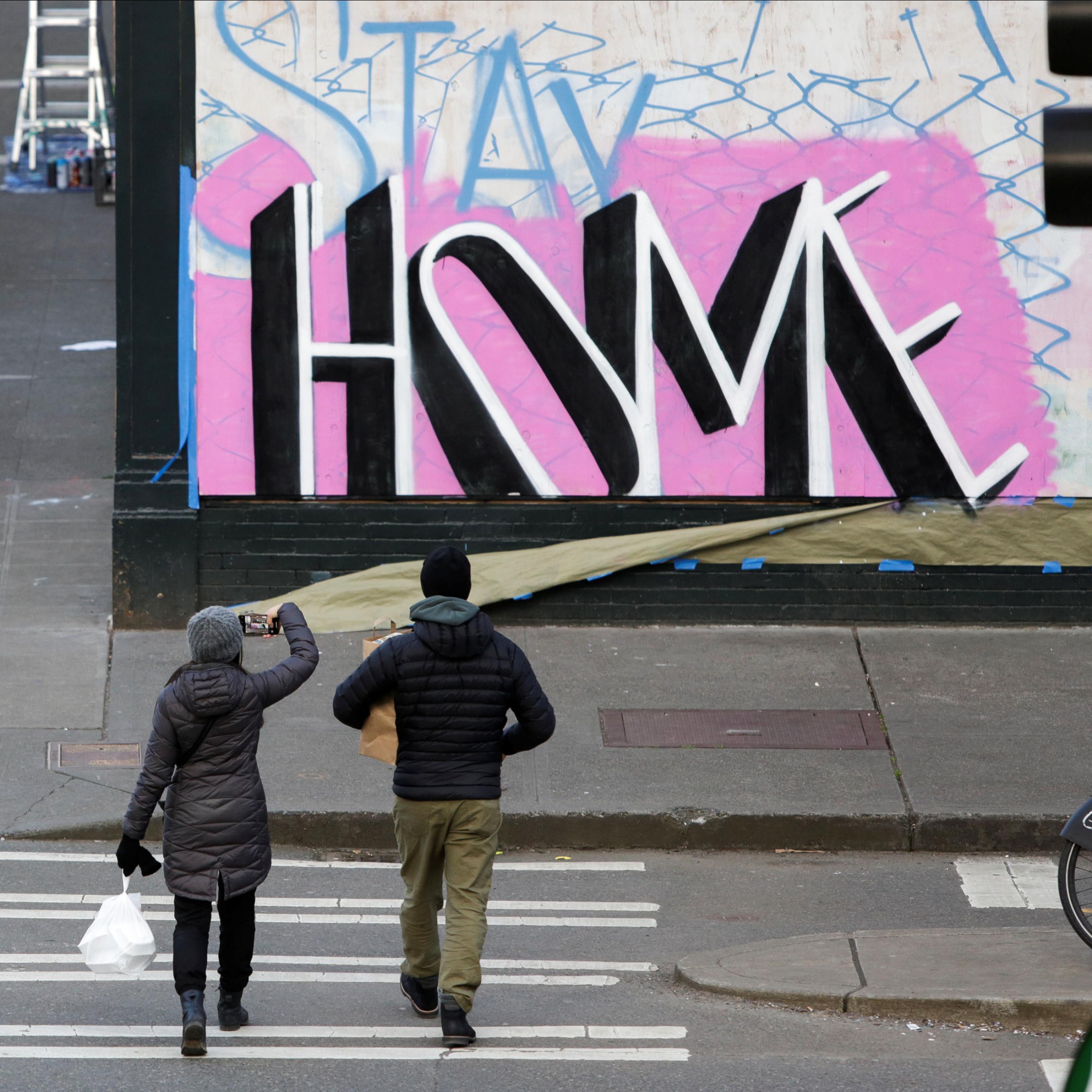 A couple totess take out food as they walk near street art with the message 