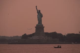 The Statue of Liberty is seen at sunset through haze caused by smoke from Canadian wildfires, as viewed from Brooklyn, New York, August 5, 2025.