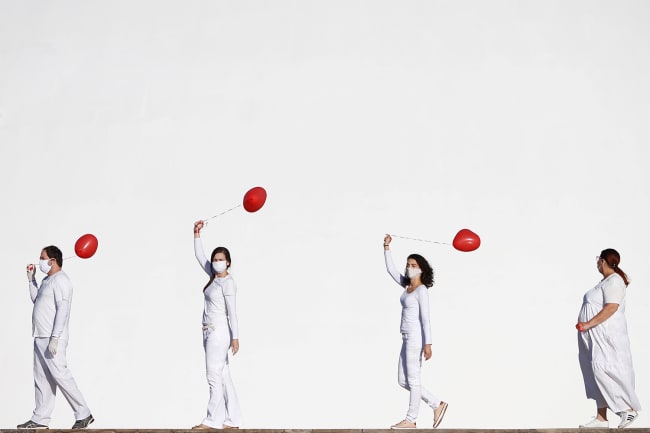 Artists perform with red balloons at a protest in honor of people who died from coronavirus disease (COVID-19) during its outbreak in Brasilia, Brazil, on June 1, 2020. The photo shows four artists dressed in white walking in front of a massive white backdrop. Each holds a red balloon. REUTERS/Adriano Machado