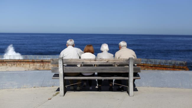A pair of elderly couples view the ocean and waves along the beach.