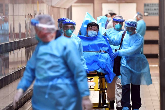 Medical staff transfer a patient of a highly suspected case of a new coronavirus at the Queen Elizabeth Hospital in Hong Kong on January 22, 2020. Picture shows a patient on a wheeled bed surrounded by four health care providers moving him with another caregiver walking in front. They all are covered head-to-toe in blue protective gear. REUTERS/cnsphoto