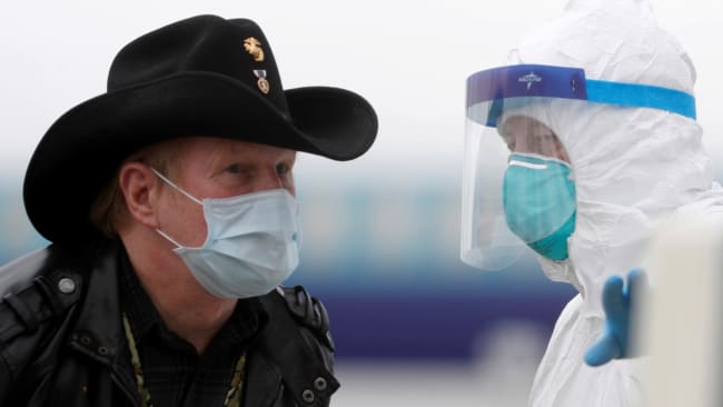 A worker in protective gear directs a masked passenger disembarking from the cruise ship Grand Princess in Oakland, California on March 10, 2020 amid concern over the growing COVID-19 pandemic. The picture shows a man wearing a mask and a cowboy hat standing facing a health worker in full protective gear. REUTERS/Stephen Lam 