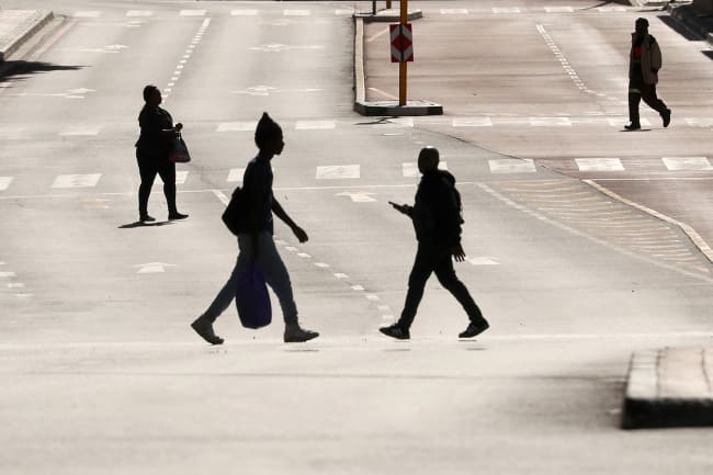 People cross normally busy—now largely empty—Adderley Street in central Cape Town, South Africa, on April 14, 2020, during the 21-day nationwide lockdown aimed at limiting the spread of coronavirus. This is a stunning photo showing a broad main thoroughfare that is completely bereft of cars. Four people are seen crossing the wide street, each silhouetted against the early or late sun reflecting off the asphalt pavement. REUTERS/Mike Hutchings
