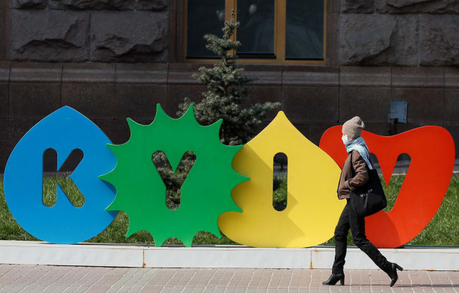 A woman wearing a mask during the coronavirus pandemic walks along the empty main street Khreshchatyk in central Kyiv, Ukraine on March 30, 2020—a colorful sign behind her bears the name of the city. This is a striking photo with a stylish woman walking in front of a sign with the city's name. REUTERS/Gleb Garanich