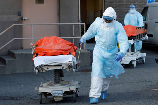 Health care workers wheel the bodies of deceased people from the Wyckoff Heights Medical Center during the coronavirus outbreak in the Brooklyn borough of New York City on April 4, 2020. The photo shows two people in blue protective suits wheeling people away from a hospital entrance. REUTERS/Andrew Kelly