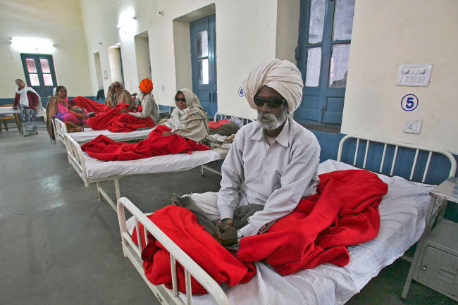 People waiting for treatment at a hospital after undergoing cataract removals from a free but shoddy eye surgery camp that caused them to lose their vision—in Amritsar, India, on December 5, 2014. The photo shows several people sitting on hospital beds. One man in the foreground is wearing dark glasses. REUTERS/Munish Sharma