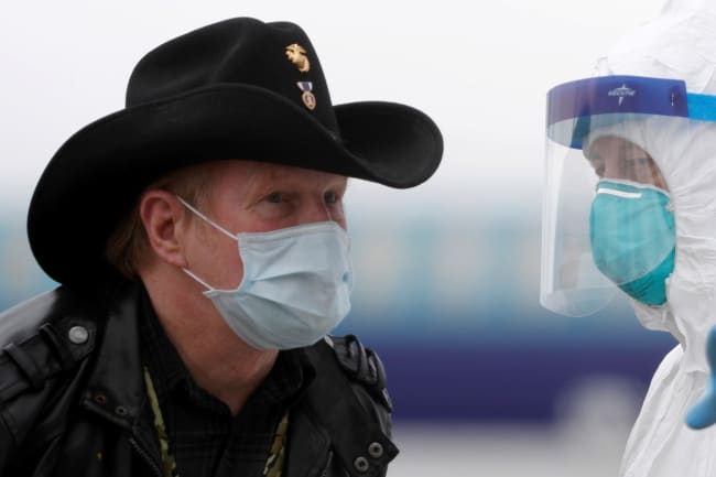 A worker in protective gear directs a masked passenger disembarking from the cruise ship Grand Princess in Oakland, California on March 10, 2020 amid concern over the growing COVID-19 pandemic. The picture shows a man wearing a mask and a cowboy hat standing facing a health worker in full protective gear. REUTERS/Stephen Lam 