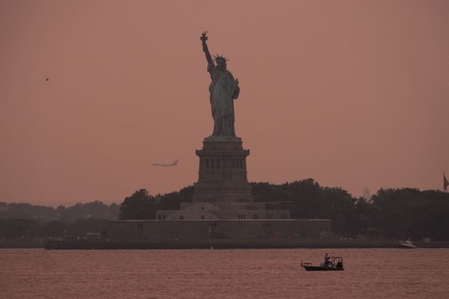 The Statue of Liberty is seen at sunset through haze caused by smoke from Canadian wildfires, as viewed from Brooklyn, New York, August 5, 2025.