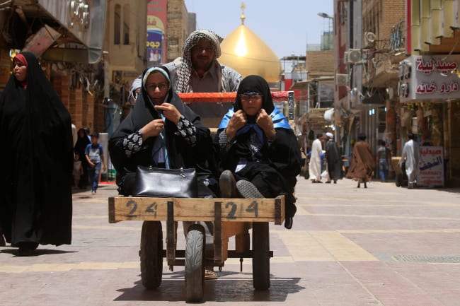 A man pushes a cart to transport women in Najaf, Iraq.