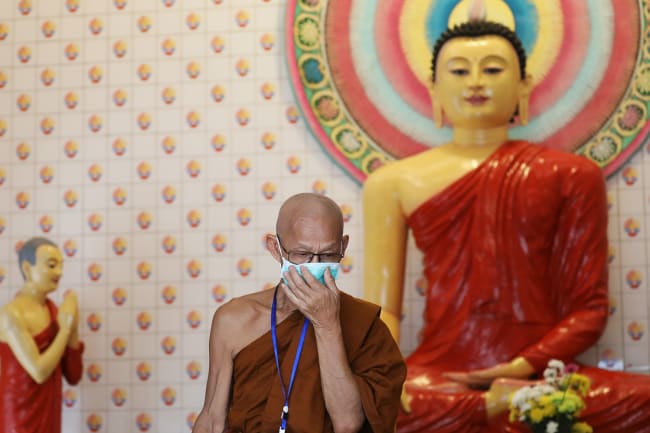 A Buddhist monk adjusts his protective face mask before a blessing ceremony for the people affected by the COVID-19 coronavirus outbreak, at a temple in Kuala Lumpur, Malaysia on February 22, 2020. This is a striking image with the monk in the foreground and some very colourful Buddhist temple features in the background. REUTERS/Lim Huey Teng