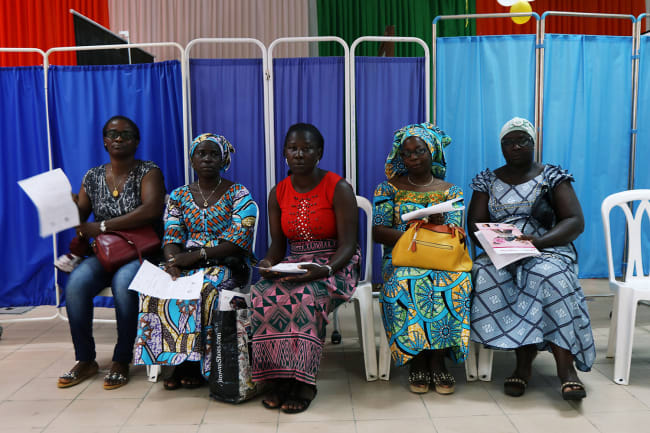 Women sit as they prepare for screenings during the breast cancer prevention campaign in Abidjan, Ivory Coast on October 12, 2019. Image shows a row of several women wearing colorful clothes. REUTERS/Luc Gnago