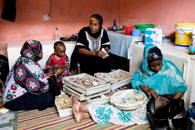 Traditional healer Bi Mwanahija Mzee folds root medicine in a piece of paper to give to a mother who complains of her child's constipation in Zanzibar City, Tanzania on January 31, 2019. The photo shows the healer facing the camera and sitting between two other women and a child. REUTERS/Nicky Woo