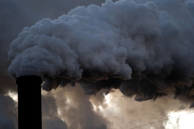 A boiler stack at the Sugar Cane Growers cooperative in Belle Glade, Florida on January 6, 2010. The image shows a large smokestack belching out black billows and blocking the cloudy sky. 