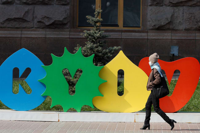 A woman wearing a mask during the coronavirus pandemic walks along the empty main street Khreshchatyk in central Kyiv, Ukraine on March 30, 2020—a colorful sign behind her bears the name of the city. This is a striking photo with a stylish woman walking in front of a sign with the city's name. REUTERS/Gleb Garanich
