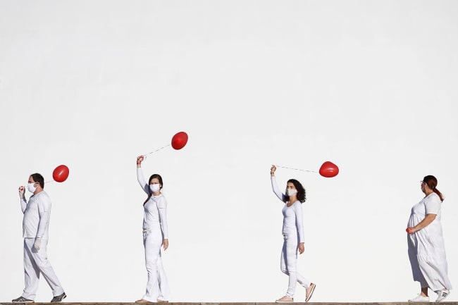 Artists perform with red balloons at a protest in honor of people who died from coronavirus disease (COVID-19) during its outbreak in Brasilia, Brazil, on June 1, 2020. The photo shows four artists dressed in white walking in front of a massive white backdrop. Each holds a red balloon. REUTERS/Adriano Machado