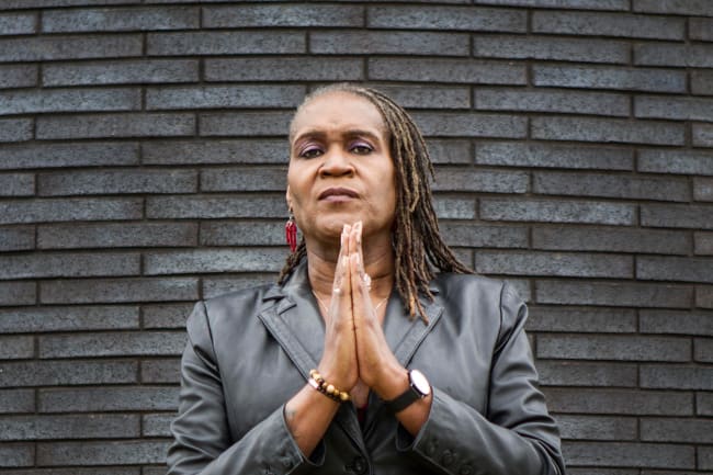 The photo shows the council vice president standing in front of a slate-colored brick wall with her hands together looking at the camera. 