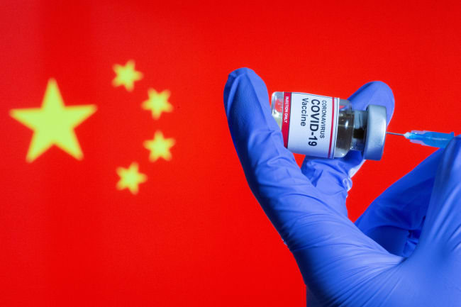 A woman holds a small bottle labeled with a "Coronavirus COVID-19 Vaccine" sticker and a medical syringe in front of displayed China flag in this illustration taken, October 30, 2020.