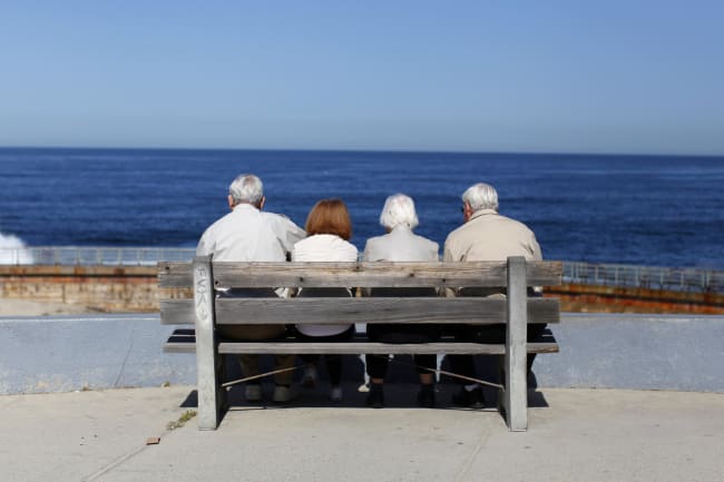 A pair of elderly couples view the ocean and waves along the beach.