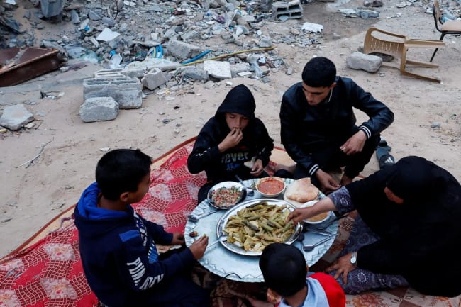 A Palestinian family eats their iftar meal they break their fast near the rubble of their destroyed house.