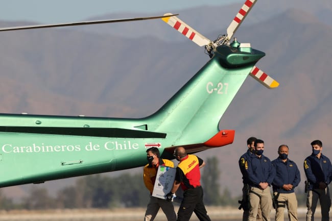Workers carry a batch of the Pfizer-BioNTech COVID-19 vaccine to a helicopter.