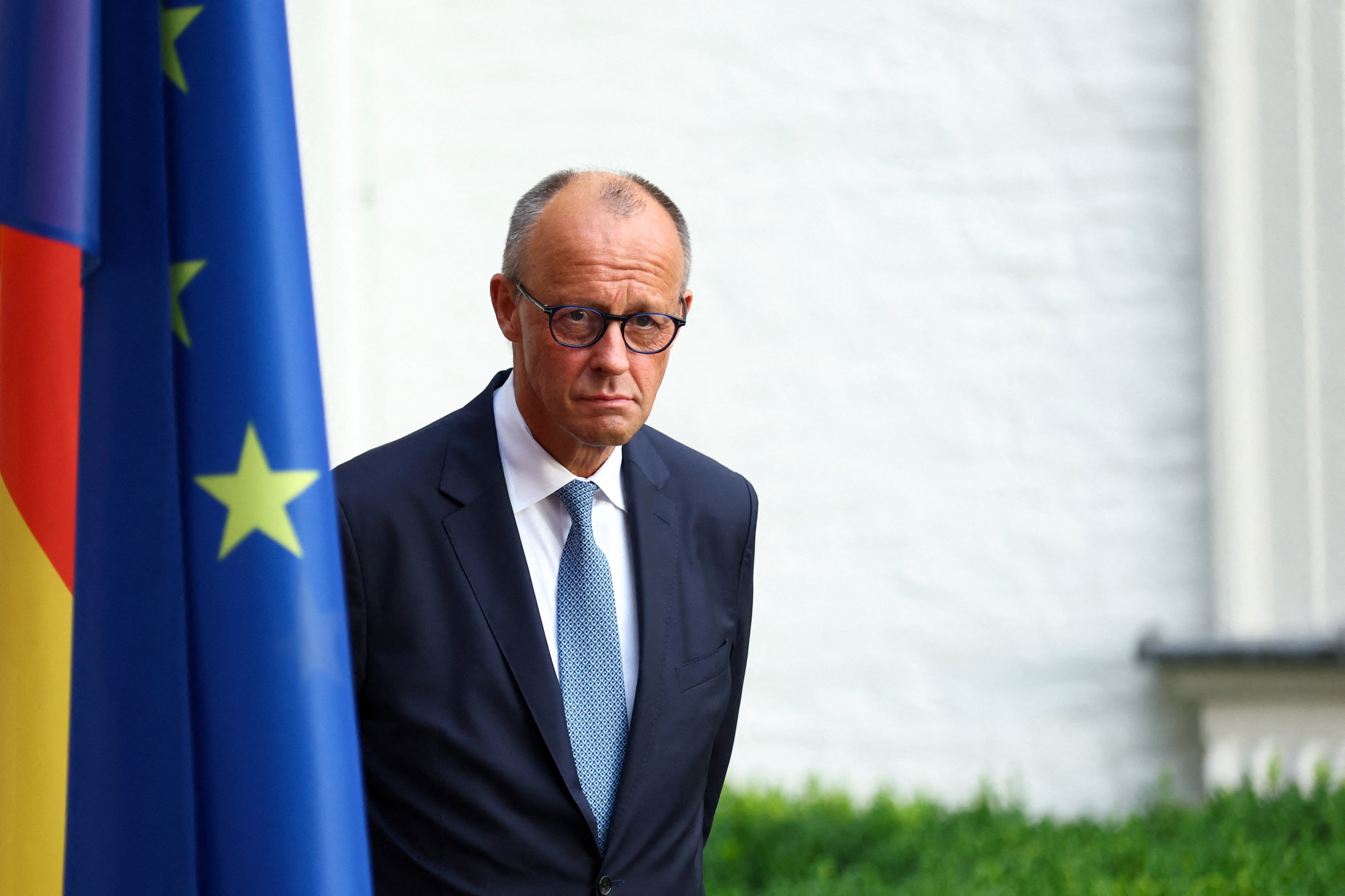 German Chancellor Friedrich Merz stands behind two flags outside the Grandhotel Schloss Bensberg in Bensberg, Germany, July 16, 2026.