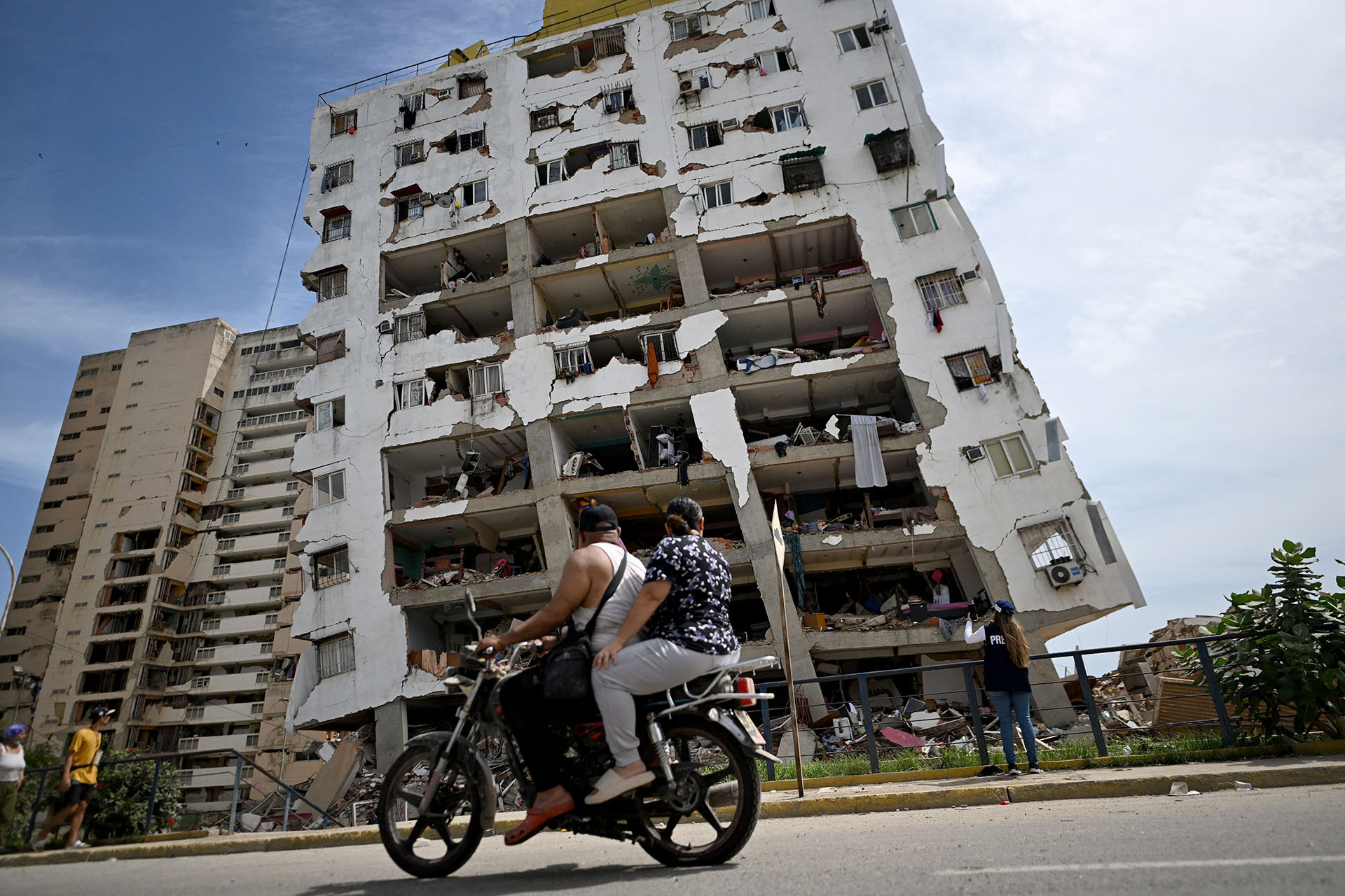 Two people ride a motorcycle past a heavily damaged apartment building with its facade torn open following an earthquake in Catia La Mar, La Guaira state, about 30 km northwest of Caracas, on June 25, 2026.