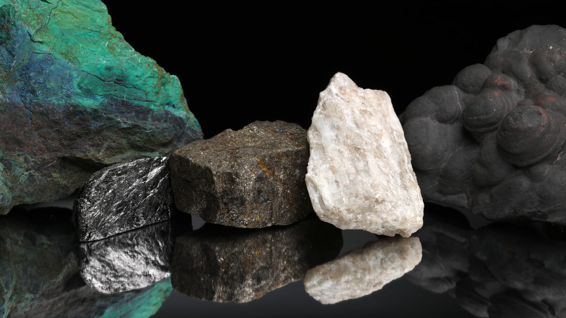 Critical mineral ores, including copper, graphite, nickel, lithium, and manganese, against a black background and reflected on a mirrored table.