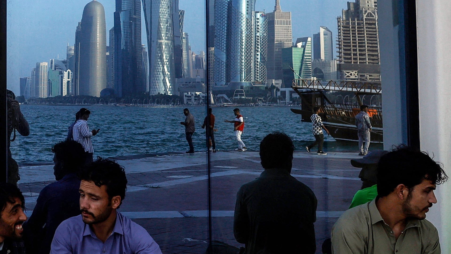 People sit with the reflection of the Doha skyline along the Doha Corniche, on the second day of Eid al-Fitr celebrations marking the end of the Muslim holy month of Ramadan, in Doha on March 21, 2026.