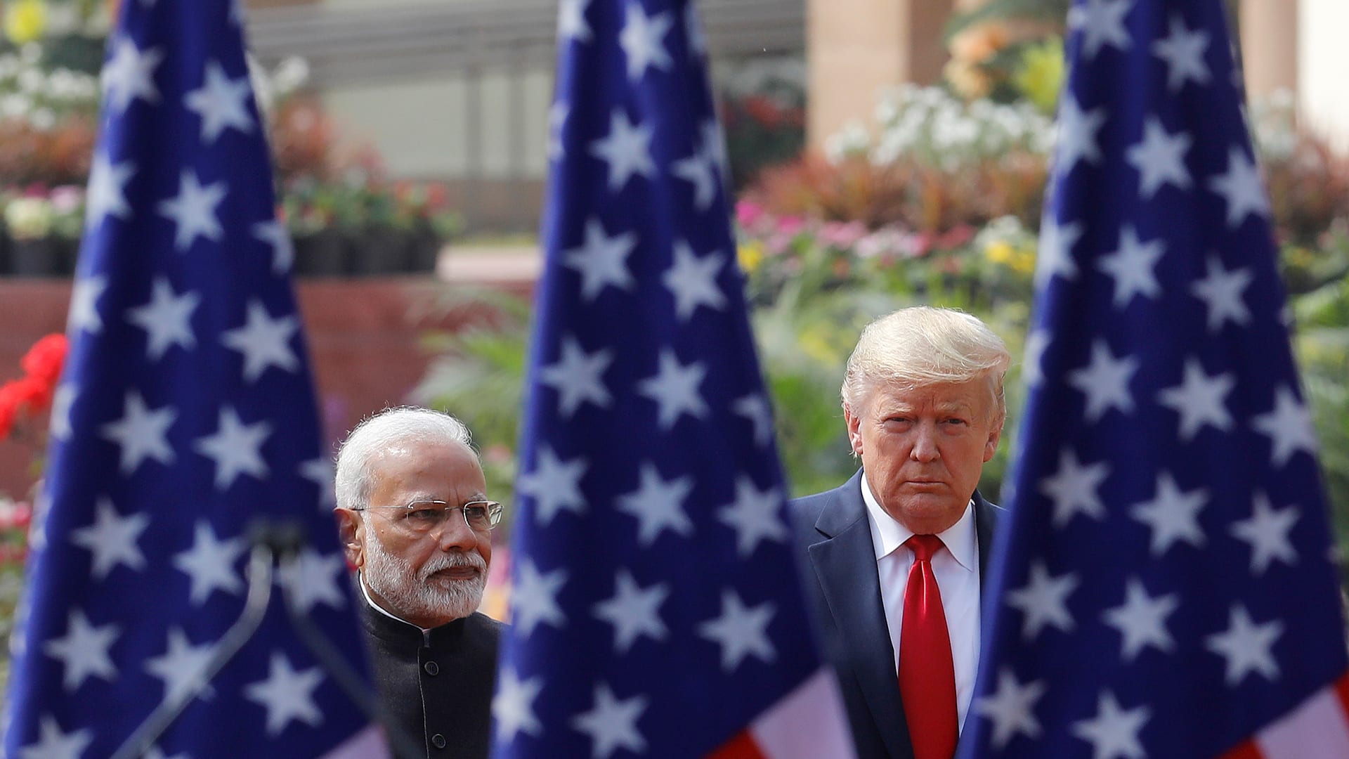 Narendra Modi and Donald Trump face the camera, separated and framed by three U.S. flags.