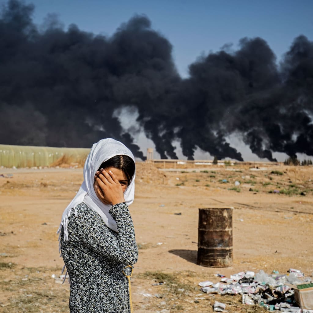 <p>A woman covers her face as she stands on the outskirts of a town near the Syria-Turkey border, while smoke plumes meant to decrease visibility for Turkish warplanes billow from tire fires during a cross-border offensive, on October 16, 2019.</p>
