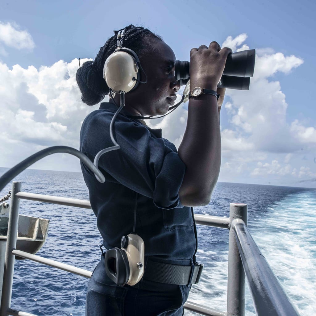<p>A seawoman uses binoculars while standing aboard the U.S. Navy aircraft carrier USS Ronald Reagan.</p>
