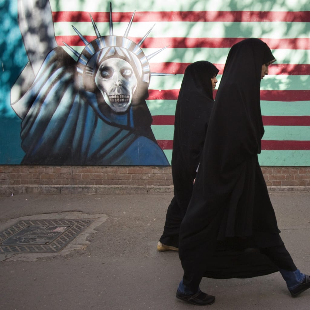 <p>Two Iranian women walk past a mural in Tehran.</p>
